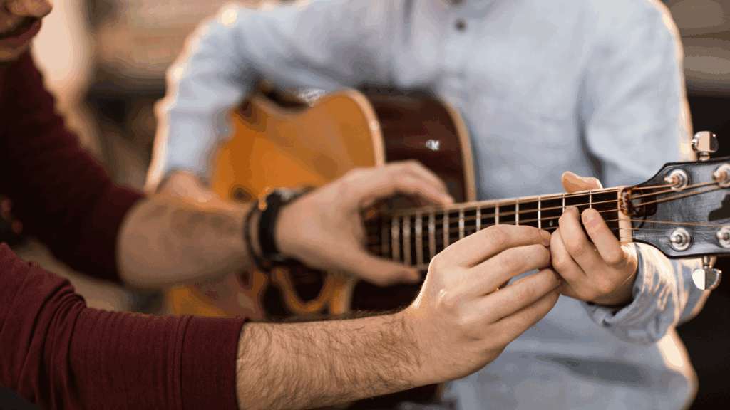Close-up view of hands guiding a student on guitar finger placement, emphasizing the importance of one-on-one instruction in music education.