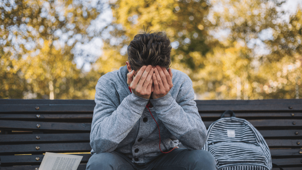 A man sitting on a park bench with his head in his hands, expressing stress or emotional distress.