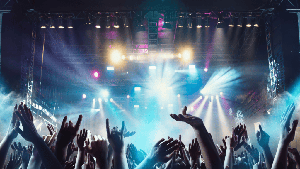 Colorful concert lights illuminating a crowd with hands raised in the air.
