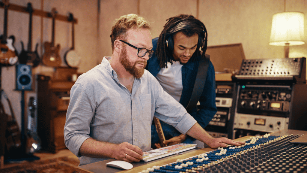 Two men in a professional music studio working on a mixing console.