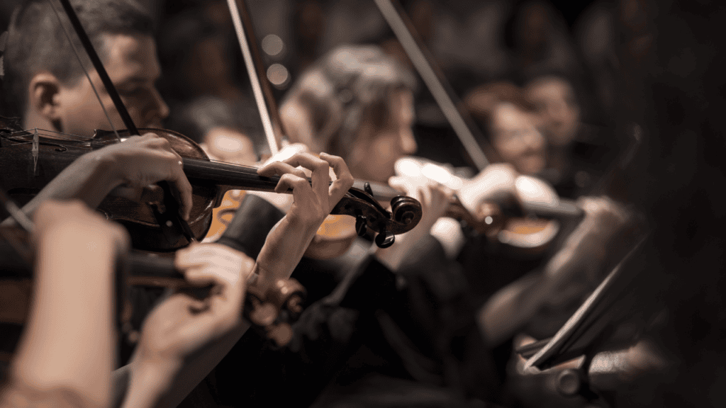 Orchestra members playing violins in a live performance.