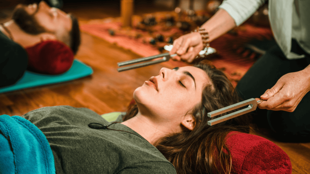 Woman lying down while experiencing sound healing with tuning forks.