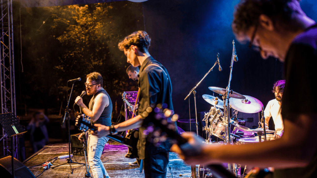 A rock band passionately performing under bright stage lights, with instruments including drums, guitar, and a microphone.