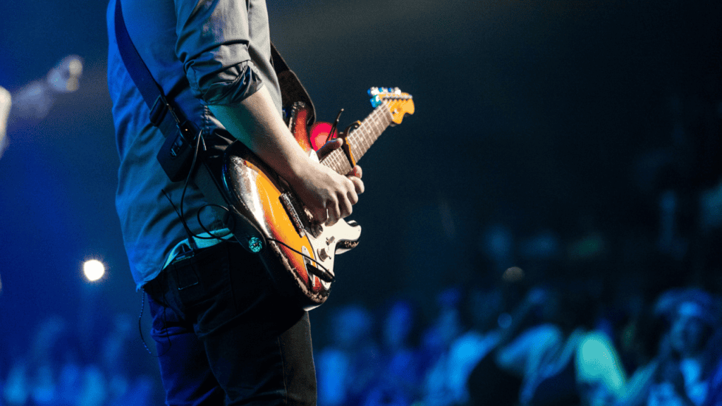 A close-up of a guitarist playing under vibrant blue lighting during a live concert.