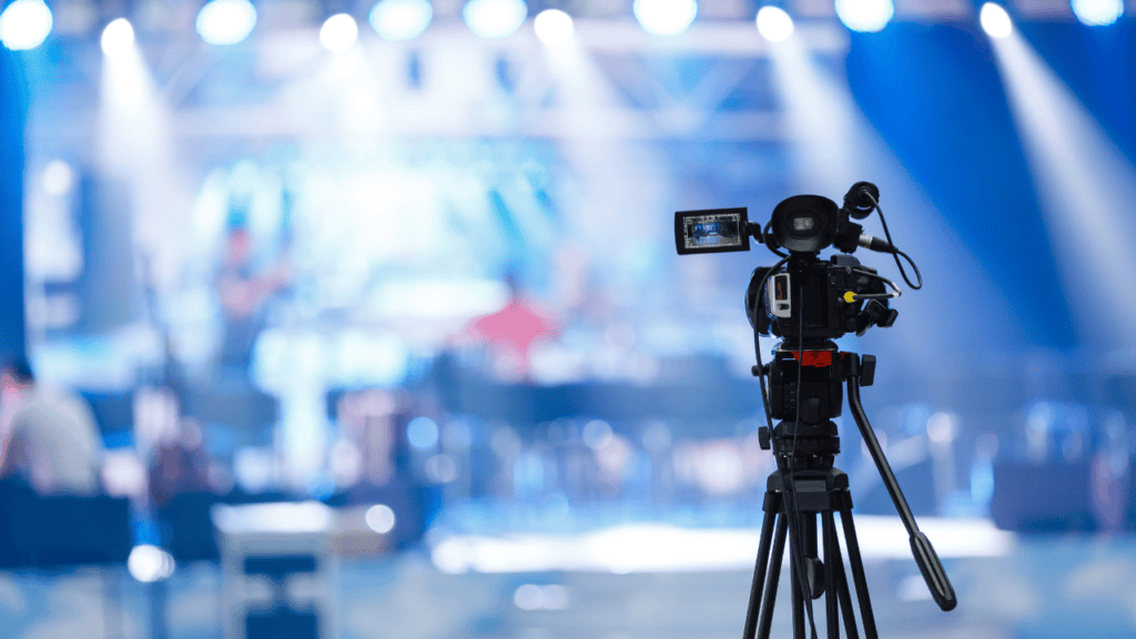 A professional video camera set up at a live music event, capturing the vibrant atmosphere of a performance.