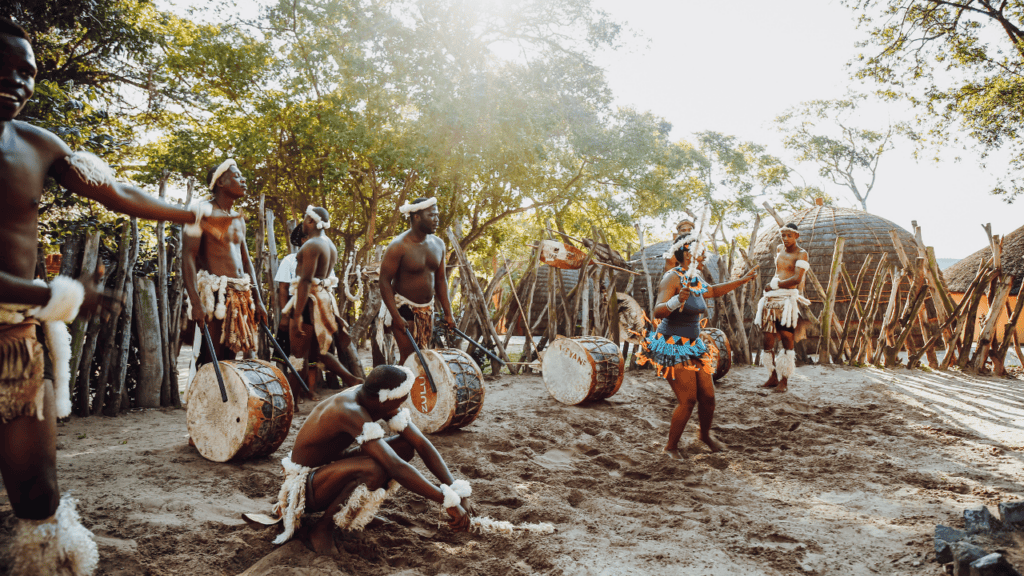 A group of men in traditional attire playing drums in a South African setting.