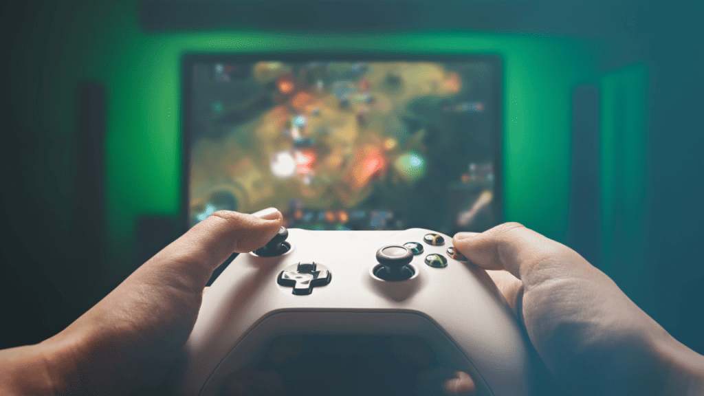 Hands holding a gaming controller in front of a blurred gaming screen.