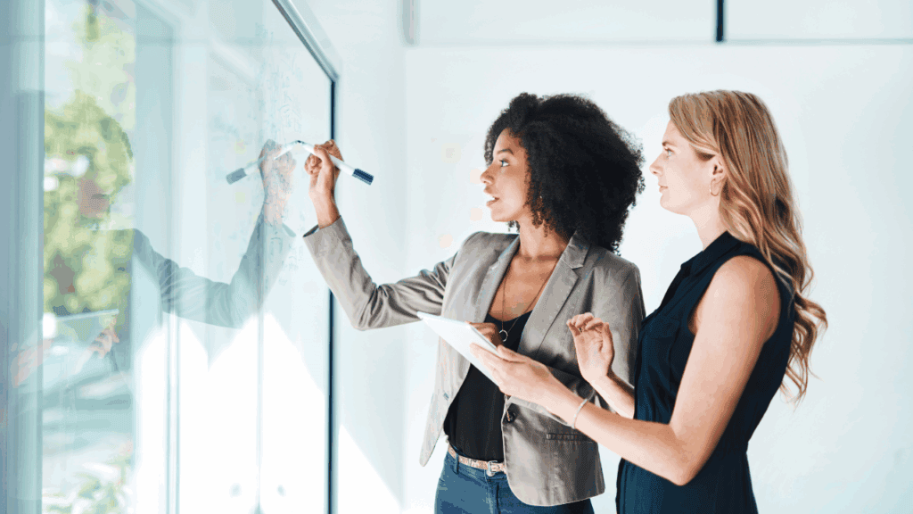 Two women discussing a strategy on a whiteboard in a modern office