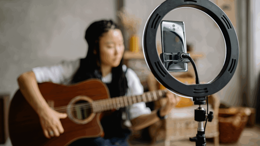 Female musician performing guitar in front of a smartphone with ring light setup.