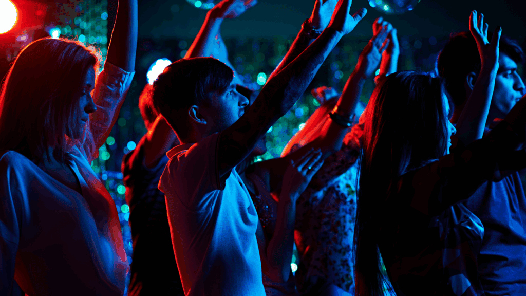 Young people dancing and raising hands at a nightclub with neon lighting