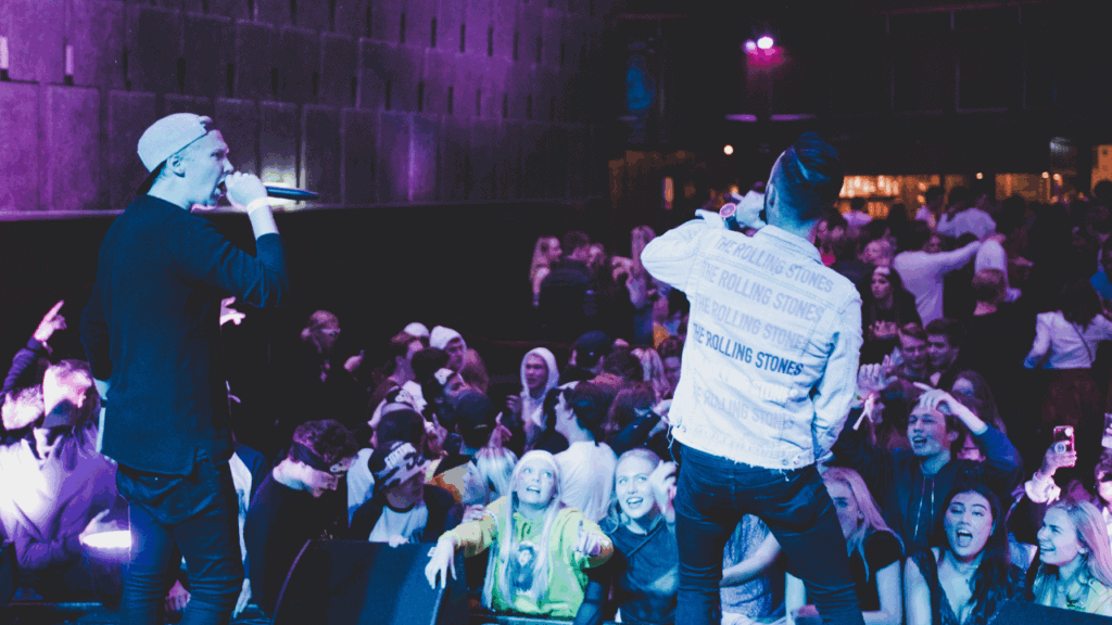 Two hip-hop artists performing on stage in front of an excited crowd