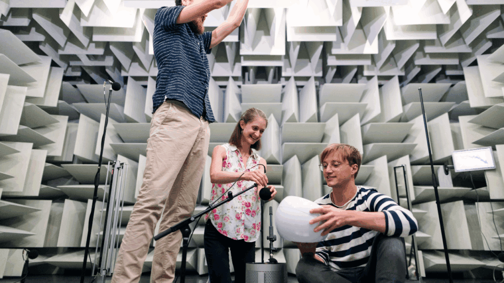 Three people testing acoustic treatment in a professional anechoic chamber with foam panels